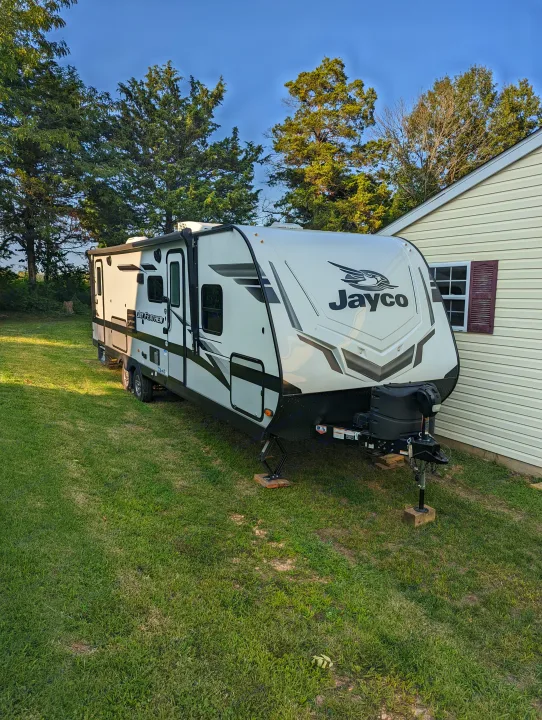 This Jayco Jay Feather travel trailer, ideal for an rv rental, is parked on a lush green lawn next to a house.. Jayco Jay Feather 2022