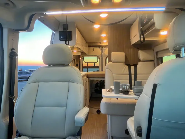 Comfortable RV rental interior featuring light-colored seating, a dining table with place settings, and a beautiful sunset view.. Thor Rize 2022