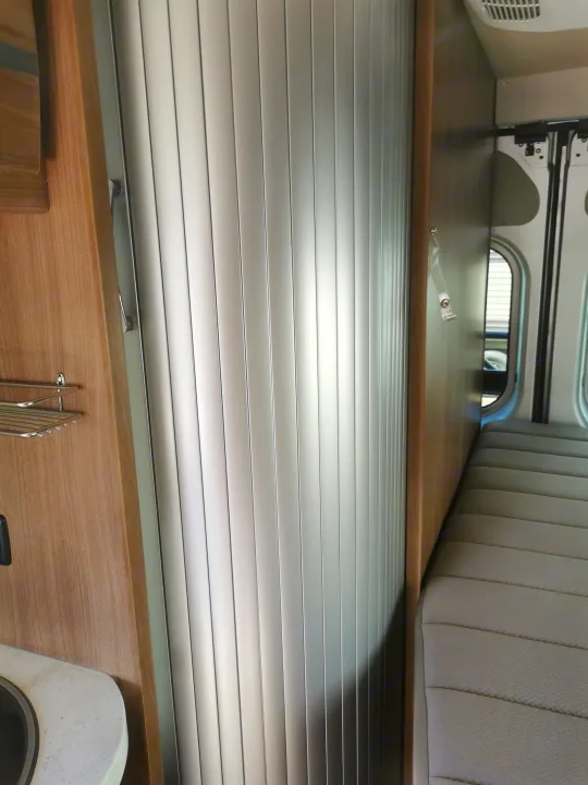 RV rental interior: A closed silver tambour door, wooden cabinets, a sink area, and grey upholstered seating. Compact design.. Winnebago Travato 2018