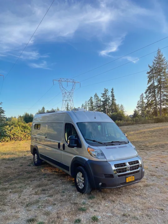 Explore with this silver RV rental camper van, parked in a clearing near power lines and tall trees under a blue sky.. Dodge Other 2018