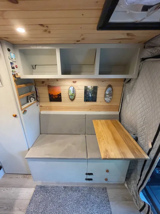 An RV rental's inviting dinette setup: light wood, wall art, gray bench seating, practical wooden table & overhead storage.. Dodge Other 2018