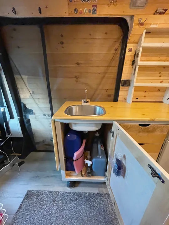 Compact RV rental kitchen with sink and clever water storage in a wood-paneled camper van interior.. Dodge Other 2018