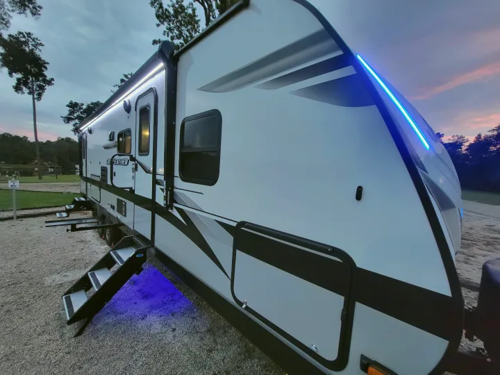 Beautiful rv rental lit up at dusk, with blue accents and white awning lights, steps extended at campsite.. Jayco Jay Feather 2023