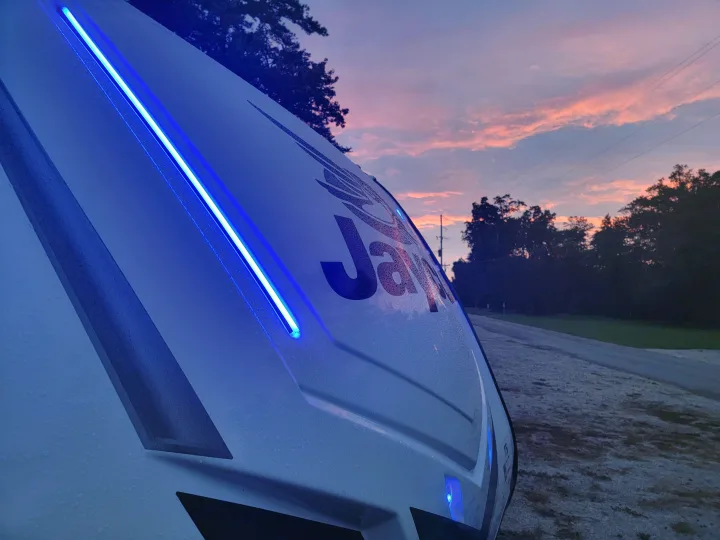 Jayco RV rental shimmering with blue lights and water droplets against a gorgeous pink and purple sunset.. Jayco Jay Feather 2023