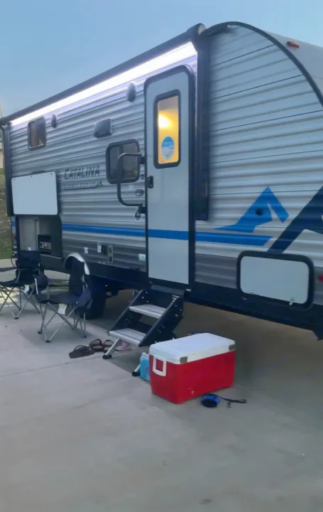 This Catalina RV rental travel trailer is set up for camping. Awning lights, chairs, cooler, and steps are outside.. Coachmen Catalina Summit Series 7 2022