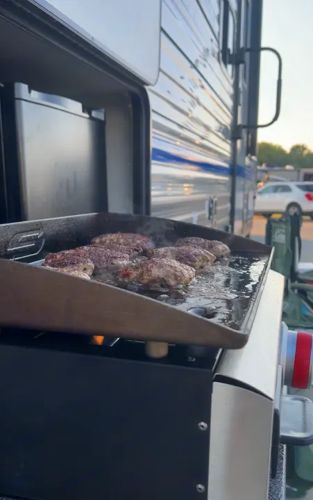 Sizzling burgers on a griddle next to an RV rental. Ideal outdoor cooking for your trip.. Coachmen Catalina Summit Series 7 2022