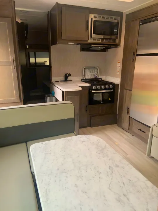 RV rental interior: Kitchen with microwave, stove, fridge, sink, and dining booth with a marble-look table.. Coachmen Leprechaun 2022