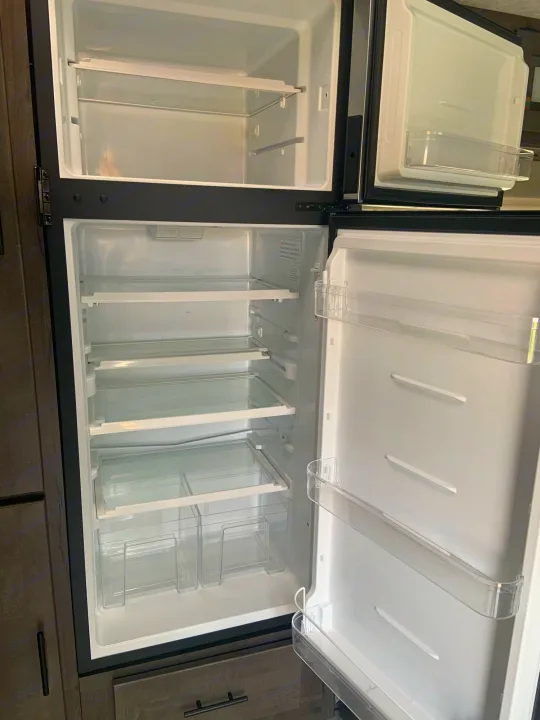 Clean, empty RV rental refrigerator and freezer, ready for your adventures. Shows interior shelves and door storage bins.. Coachmen Leprechaun 2022