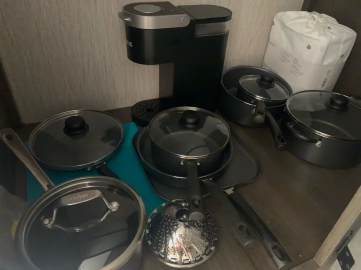 Essential kitchen setup in an RV rental: a coffee maker, various pots and pans with lids, a griddle, steamer, and a linen pack.. Coachmen Leprechaun 2022