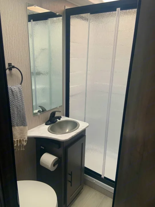 Compact RV rental bathroom with a modern sink, toilet, and glass shower for convenient travel.. Coachmen Leprechaun 2022