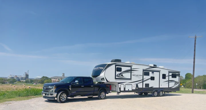 Black pickup truck tows a white Grand Design Reflection fifth-wheel RV rental, parked on a sunny day.. Grand Design Reflection 2021