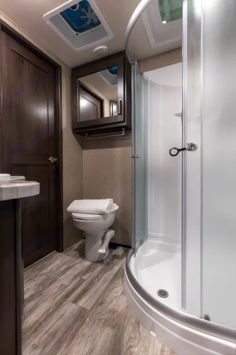 Explore this RV rental bathroom: compact design with curved shower, toilet, vanity, and wood-look flooring.. Grand Design Reflection 2021