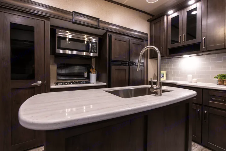 Well-equipped RV rental kitchen interior: dark wood, modern appliances, island sink, and light countertops.. Grand Design Reflection 2021