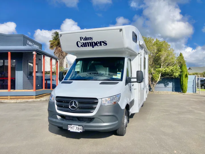 A white Mercedes-Benz campervan with 'Palmy Campers' branding, available for RV rental, parked on an asphalt lot.. Mercedes-Benz Sprinter 2022