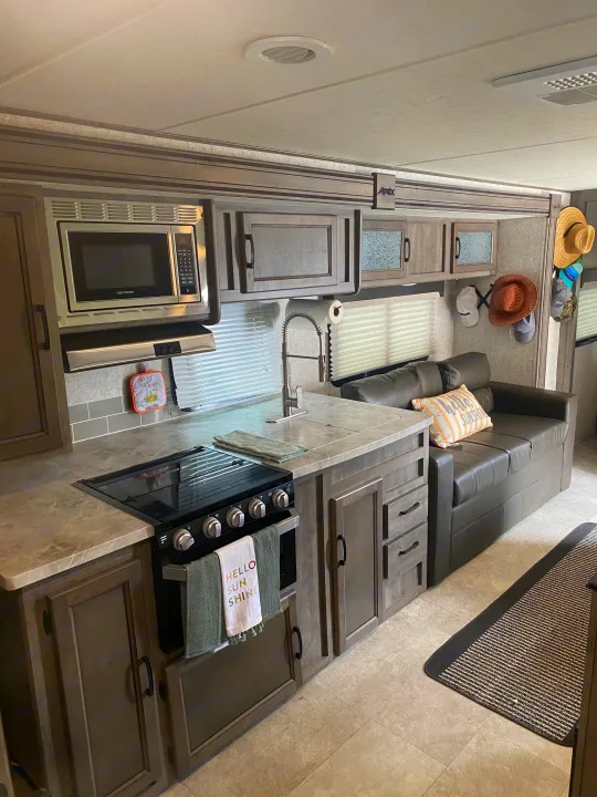 This RV rental offers a well-equipped kitchen area with microwave, stove, and sink, next to a comfortable sofa in the living space.. Coachmen Apex 2019