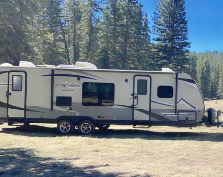 This sleek Apex Ultra Lite RV rental is parked in a sunny, forested campground, ideal for outdoor adventures.. Coachmen Apex 2019