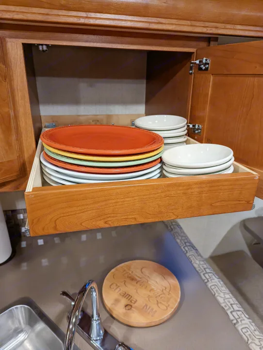 Optimized RV rental kitchen storage: a pull-out drawer with colorful plates and bowls in a wooden cabinet, above a sink.. Winnebago Vista 2018