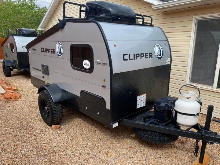 Two gray and black Clipper travel trailers, with roof racks and all-terrain tires, are parked on gravel, ideal for an RV rental.. Coachmen Clipper Express 9.0 TD 2022