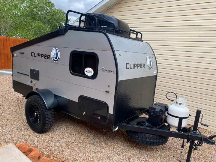 A rugged Coachmen Clipper travel trailer, ready for an rv rental adventure, with off-road tires, propane tank, and roof storage.. Coachmen Clipper Express 9.0 TD 2022