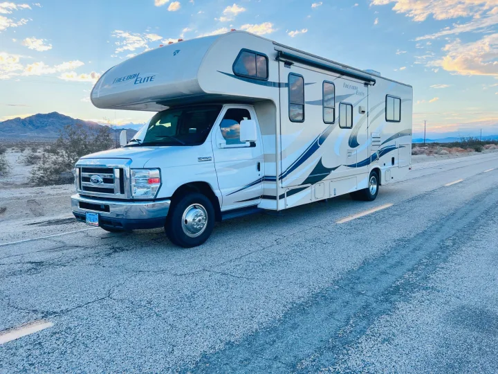 A white Ford E-450 Freedom Elite RV rental parked on a desert road at sunset. Perfect for your next scenic adventure.. Thor Freedom Elite 2015