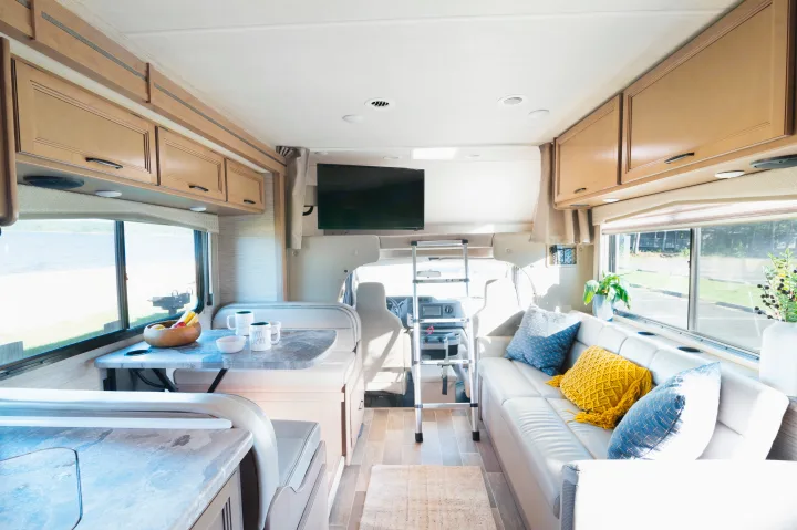 Spacious RV rental interior featuring a dining area, cozy lounge with pillows, kitchen counter, and driver's cabin view.. Thor Chateau 2022