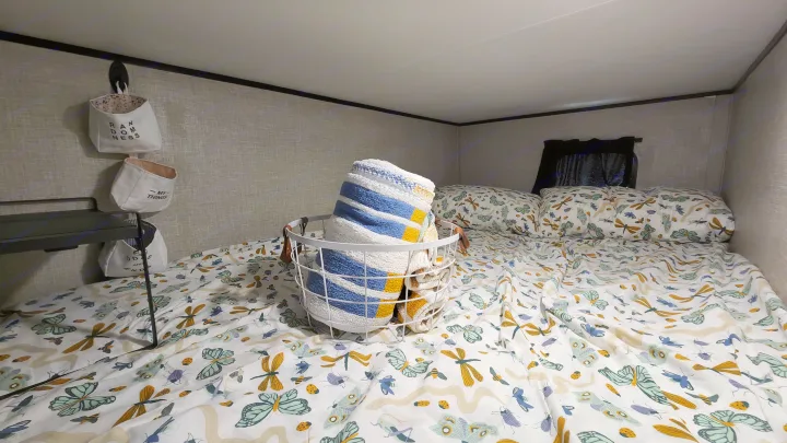 Cozy RV rental bunk bed with insect-patterned bedding, a rolled blanket, and wall storage baskets for a comfortable stay.. Jayco Jay Flight SLX 2022