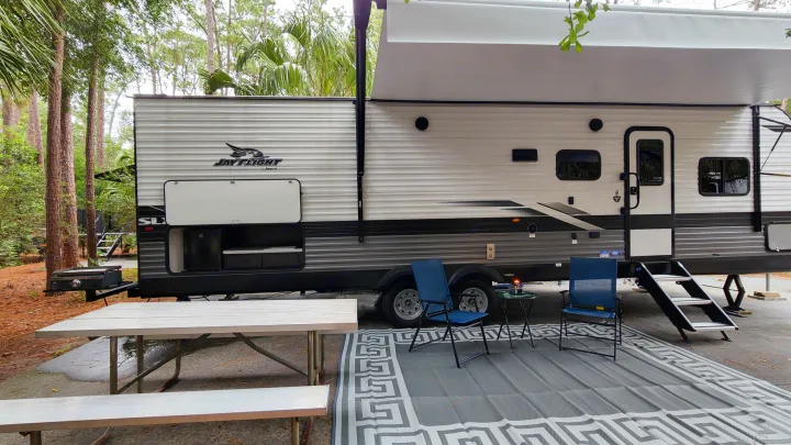RV rental setup at a shaded campsite, featuring an extended awning, picnic table, chairs, and outdoor kitchen for comfortable outdoor living.. Jayco Jay Flight SLX 2022