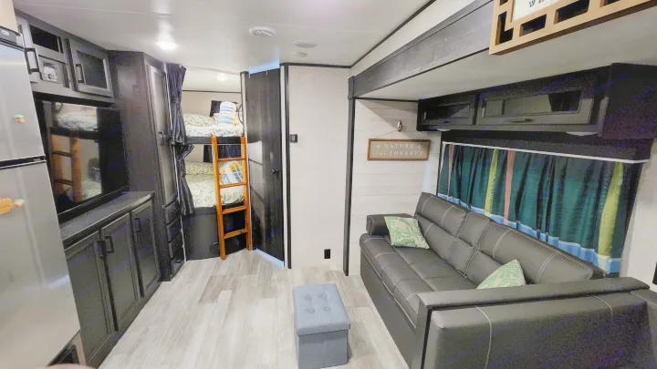 Inside an RV rental: Cozy camper interior with bunk beds, sofa, fridge, and wooden floors. "Nature is my therapy" sign.. Jayco Jay Flight SLX 2022