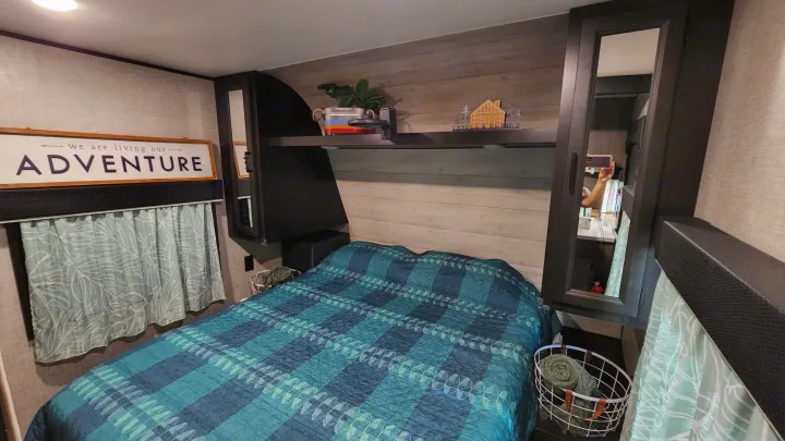 Cozy RV rental bedroom featuring a blue quilt, "ADVENTURE" sign, and built-in storage for comfortable travels.. Jayco Jay Flight SLX 2022