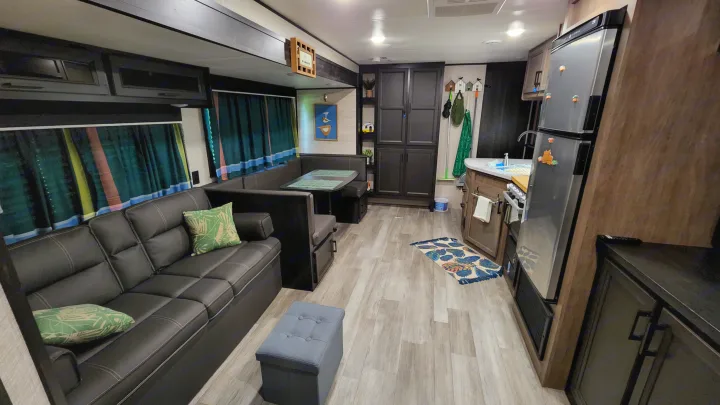 Inside this RV rental: a modern living space with black sofa, dinette, kitchen, and light wood-look flooring.. Jayco Jay Flight SLX 2022