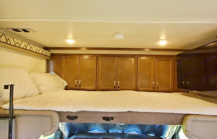 Inside an RV rental: a cozy cab-over bed with ample overhead storage cabinets and TV. Perfect for your next adventure.. Gulf Stream Conquest 2020