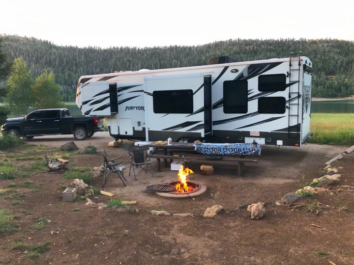 Lakeside RV rental campsite with pickup truck, picnic table, and warm campfire for outdoor fun.. Keystone Raptor 2014