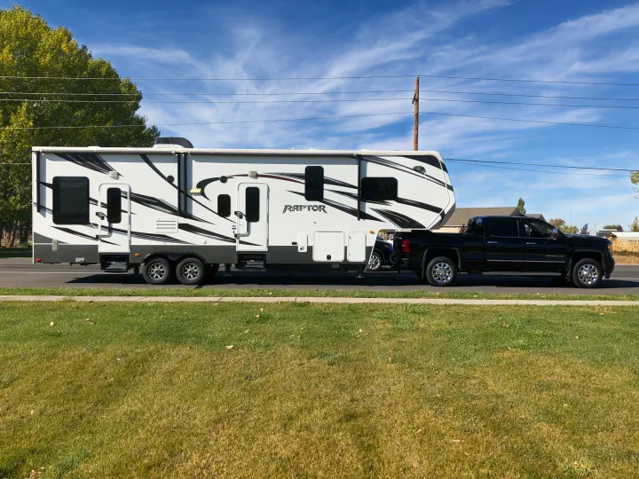 A black pickup truck tows a large white Keystone Raptor fifth-wheel RV.. Keystone Raptor 2014