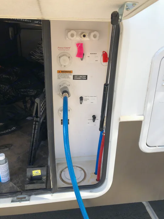 RV rental water utility bay. Blue hose connected for city water, showing winterize and tank fill controls.. Keystone Raptor 2014