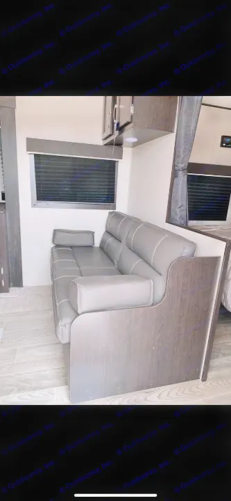 RV rental interior featuring a modern grey sofa, window with blinds, and dark wood cabinets. Great for compact living.. Jayco Jay Flight 2022