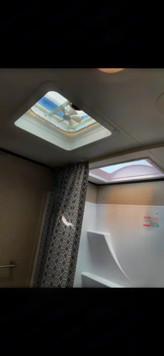 Spacious RV rental shower with skylights and a vent fan, featuring a patterned curtain and built-in seat.. Jayco Jay Flight 2022