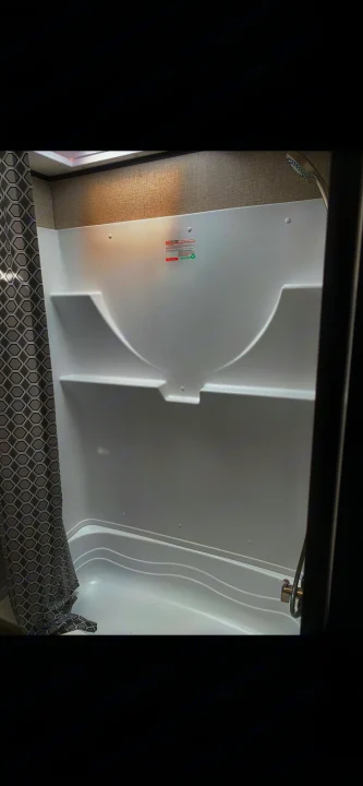 Inside an RV rental: a bright white shower/tub with molded shelves, a geometric curtain, and shower head.. Jayco Jay Flight 2022