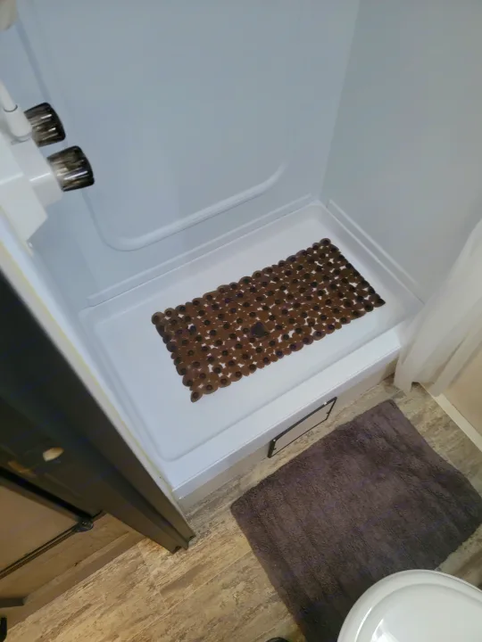 Inside an RV rental: a clean, white shower with a textured brown non-slip mat. A grey bath rug and toilet are nearby.. Keystone RV Springdale 2021