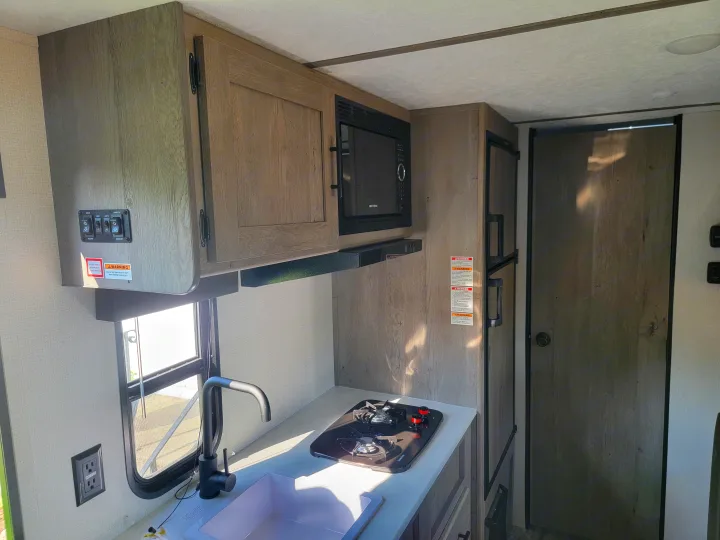 Inside a modern **rv rental**: a compact kitchen featuring a microwave, stove, sink, and refrigerator, with intuitive controls.. Keystone RV Springdale 2021