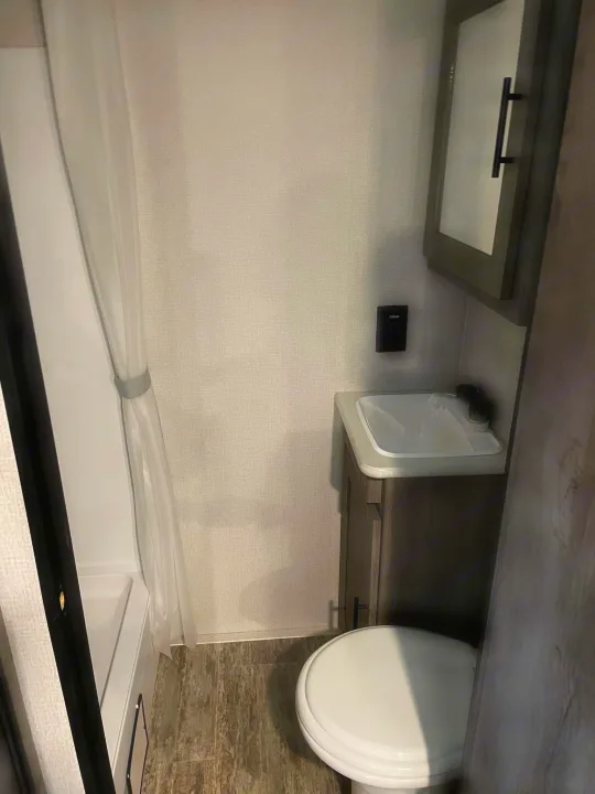 Compact RV rental bathroom with shower, toilet, and vanity. Features textured walls and tiled floor, ideal for travel.. Keystone RV Springdale 2021