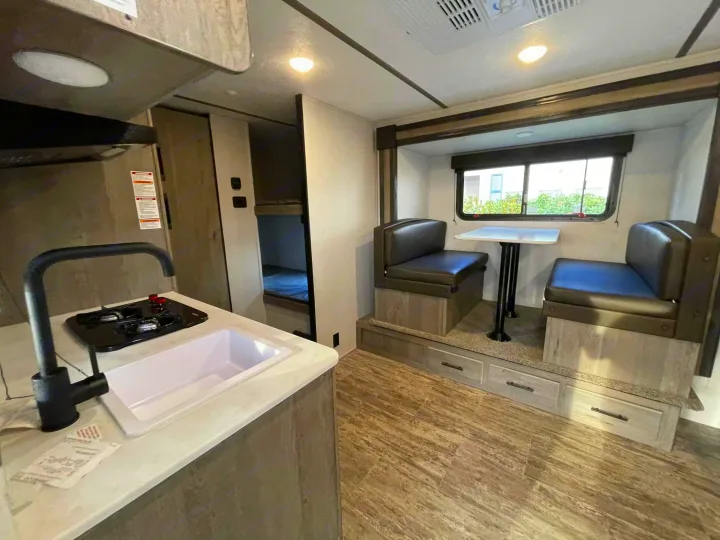 This RV rental interior features a functional kitchen, a cozy dinette booth, and bunk beds for compact living.. Keystone RV Springdale 2021