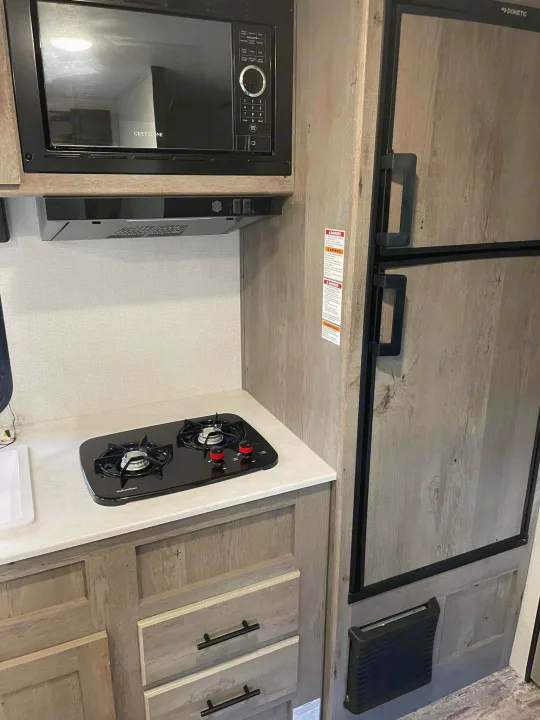 RV rental kitchen showing microwave, stovetop, Dometic fridge, and cabinets. Ready for your next adventure!. Keystone RV Springdale 2021