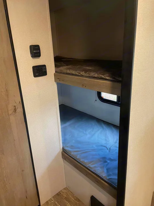 Inside an RV rental, showing compact bunk beds and wall-mounted controls for comfort and utilities.. Keystone RV Springdale 2021