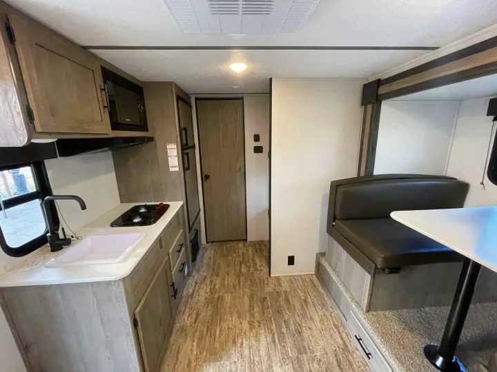 Spacious RV rental interior: modern kitchen with sink & stove, dinette booth with table, wood-look floor, and refrigerator.. Keystone RV Springdale 2021