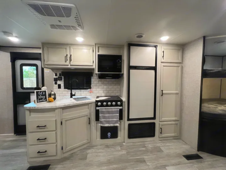 Inside an RV rental: a compact, stylish kitchen featuring a sink, stove, microwave, refrigerator, and light cabinetry. Efficient layout.. Jayco Jay Flight 267BH 2023