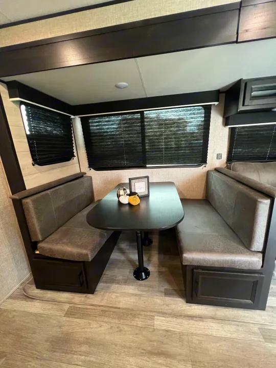 This RV rental's dinette features gray upholstered booth seats and a dark oval table, ideal for meals and relaxation.. Jayco Jay Flight 267BH 2023