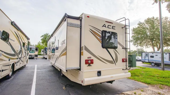 Multiple RVs, including an ACE motorhome with its slide-out extended, available for rv rental in a paved lot.. Thor A.C.E. 2020