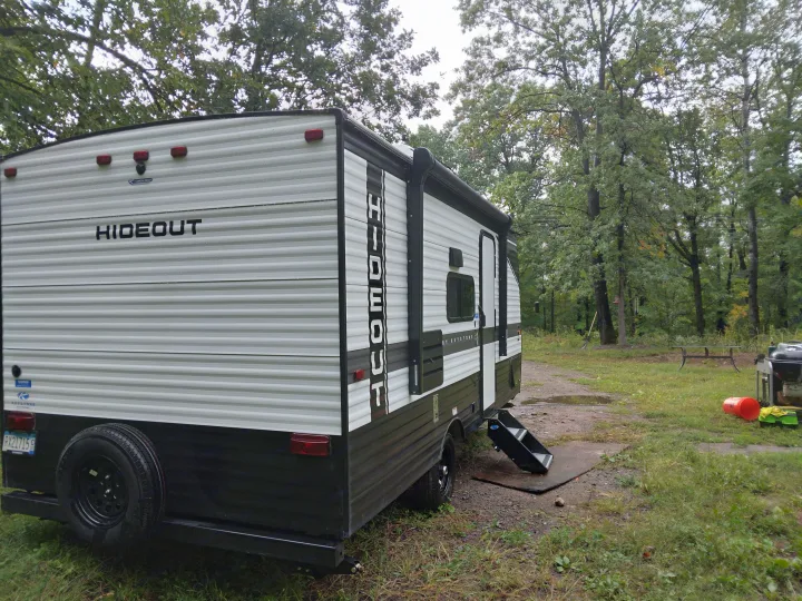 This RV rental is parked at a serene wooded campsite, ready for adventure in the great outdoors.. Keystone RV Hideout 2022