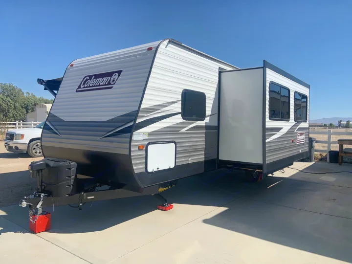 White/black Coleman travel trailer, ready for your next RV rental adventure. Slide-out extended, parked on concrete.. Dutchmen Coleman Lantern 2021