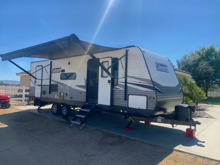 A Coleman travel trailer, with its awning extended, parked on a sunny day. Perfect for an RV rental getaway.. Dutchmen Coleman Lantern 2021